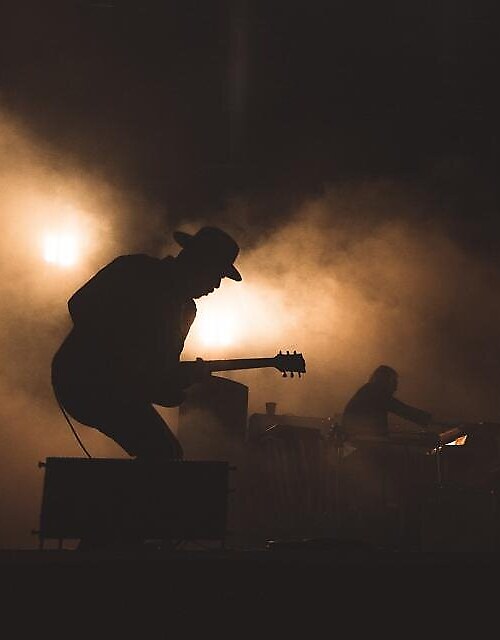 A guitarist and bandmates rehearsing under warm stage light